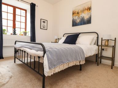 A bedroom with a metal bed frame beside a window with curtains and a side table with a lamp at Hole in the Wall in Caernarfon