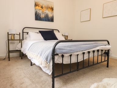 A bedroom with a black metal bed frame white bedding and a blue pillow at Hole in the Wall Caernarfon