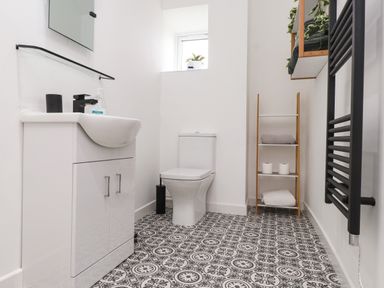 A bathroom with a white sink cabinet black towel rack and patterned floor at Hole in the Wall in Caernarfon