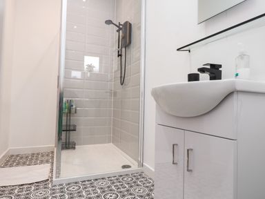 A bathroom with a shower enclosure and a white sink cabinet with black fixtures at Hole in the Wall in Caernarfon