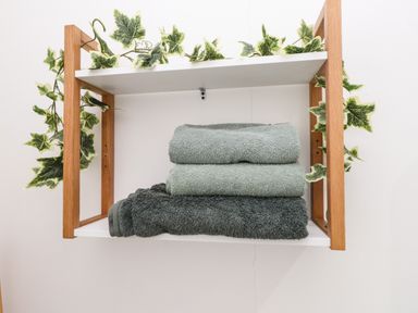 A wooden shelf with folded towels and decorative green leaves at Hole in the Wall in Caernarfon
