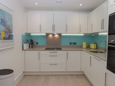 A kitchen with white cabinets a stove a sink yellow kettle and toaster and a blue backsplash at Rolles Rainbow in Exmouth