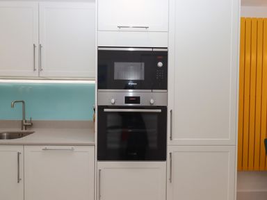 A kitchen with a sink on the left a built in microwave and oven in the center and a yellow radiator on the right at Rolles Rainbow in Exmouth