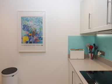A kitchen corner with a trash bin a colorful painting on the wall a set of chopping boards and utensils in holders on the counter at Rolles Rainbow in Exmouth