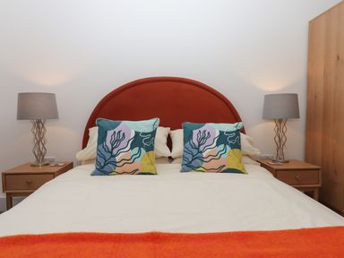 A bedroom with a red rounded headboard bed two multicolored patterned pillows two wooden nightstands with lamps and a wooden wardrobe at Rolles Rainbow in Exmouth