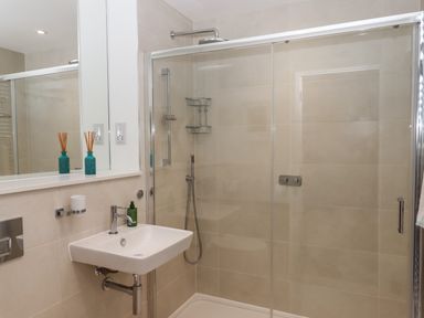 A bathroom with a wall-mounted sink, a glass-enclosed shower with a rainfall shower head and handheld shower at Rolles Rainbow in Exmouth