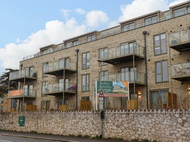 A multi-story apartment building with balconies and glass railings behind a stone wall at Rolles Rainbow in Exmouth
