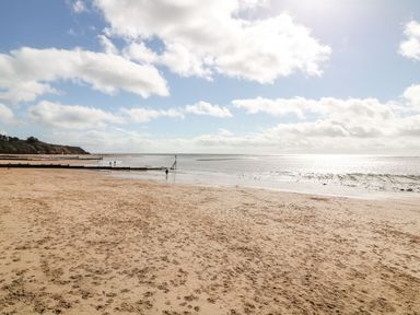 A sandy beach with footprints and wooden groynes extending into the sea under a partly cloudy sky at Rolles Rainbow in Exmouth