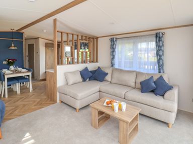 A living room with a beige sofa and blue cushions next to a wooden table with drinks and pastries at Aspen Lodge in Whitby