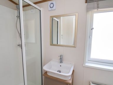 A bathroom with a shower enclosure a sink with a faucet a mirror and a window at Aspen Lodge in Whitby
