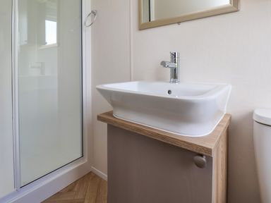 A bathroom with a sink on a wooden cabinet a shower enclosure with a glass door and a toilet at Aspen Lodge in Whitby