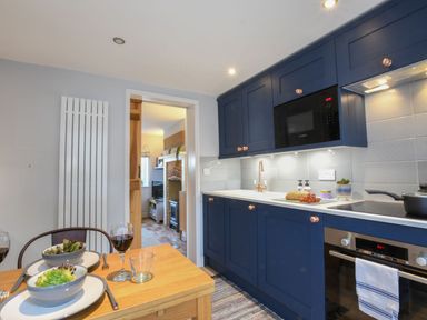 A kitchen with blue cabinets a wooden dining table set with bowls of salad and glasses of wine at Caines Cottage in Westleton