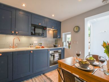 A kitchen with blue cabinets, a wooden table set with bowls of salad and glasses of wine at Caines Cottage in Westleton