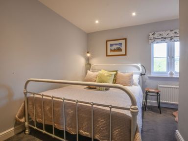 A bedroom with a metal bed frame cushions a side table and a window at Caines Cottage in Westleton