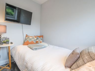 A bedroom with a bed two patterned pillows a side table lamp and a wall mounted television at Caines Cottage in Westleton