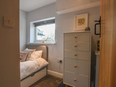 A small bedroom with a bed under a window and a tall white chest of drawers at Caines Cottage in Westleton