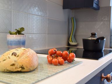 A kitchen counter with bread and cherry tomatoes next to a stove with a pot and kitchen utensils at Caines Cottage in Westleton