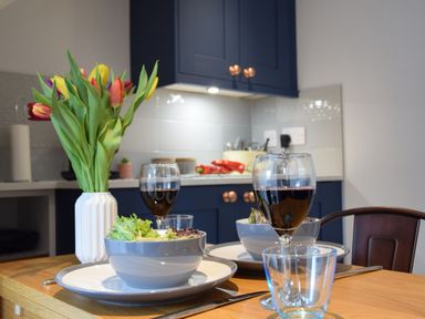 A kitchen table set with bowls of salad glasses of red wine and a vase of tulips at Caines Cottage in Westleton