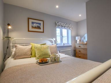 A bedroom with a white metal bed frame pillows and a tray with a teapot and croissants at Caines Cottage in Westleton