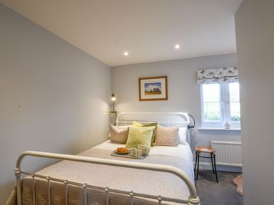 A bedroom with a bed with pillows and a tray with tea and croissants a window and a small round wooden stool at Caines Cottage Westleton