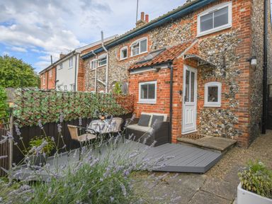 A patio with outdoor furniture and plants outside a brick and stone house at Caines Cottage in Westleton