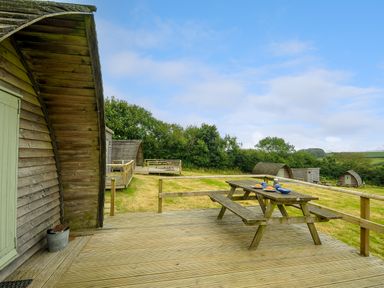 A wooden deck with a picnic table and outdoor pods in a grassy area at Hen House Penbugle Organic Farm in St Keyne near Duloe