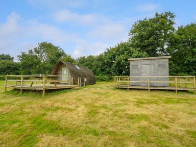 Two small wooden cabins with raised wooden decks on a grassy area with trees in the background at Hen House @ Penbugle Organic Farm in St Keyne near Duloe
