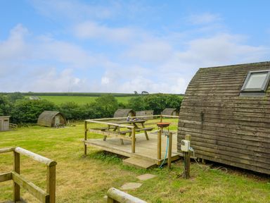 A grassy outdoor area with wooden pod cabins picnic tables and a wooden deck at Hen House Penbugle Organic Farm in St Keyne near Duloe