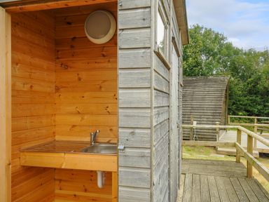 An outdoor wooden sink area next to a wooden cabin with a deck and railing surrounded by trees at Pig Pen @ Penbugle Organic Farm in St Keyne near Duloe