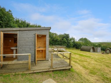 An outdoor area with wooden cabins and a wooden deck with a sink and a toilet at Pig Pen @ Penbugle Organic Farm in St Keyne near Duloe