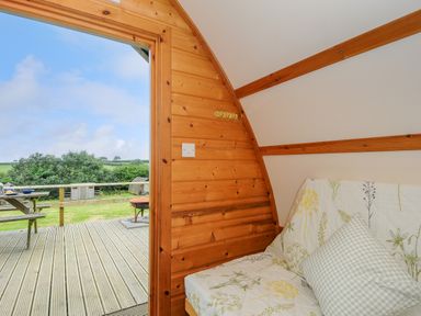 A wooden room with a floral covered sofa and an open door leading to a deck with a picnic table at Badger Set @ Penbugle Organic Farm in St Keyne near Duloe