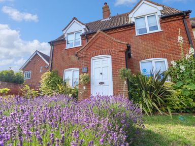A red brick house with white windows and a white door surrounded by lavender plants at 1 Market Hill in Orford