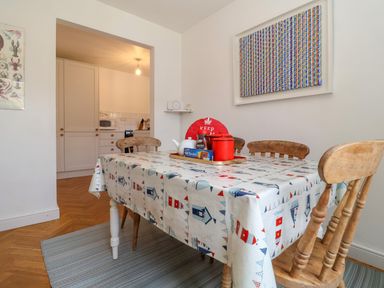 A dining area with a table covered with a printed tablecloth and wooden chairs beside a kitchen at 1 Market Hill in Orford