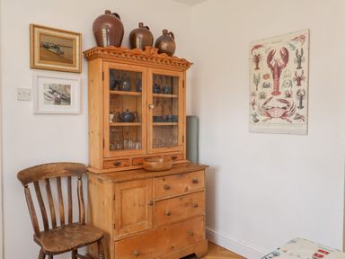 A corner of a room with a wooden cabinet holding teapots and glasses a wooden chair and framed pictures on the walls at 1 Market Hill in Orford