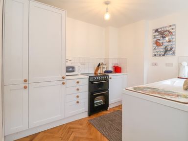 A kitchen with white cabinets a black oven a microwave and a painting of sea creatures at 1 Market Hill in Orford