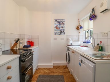 A kitchen with a black stove white cabinets a washing machine a dishwasher and a window at 1 Market Hill in Orford