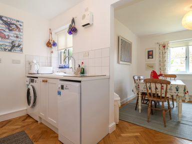 A kitchen with white cabinets dishwasher and washing machine connected to a dining area with wooden chairs and table at 1 Market Hill in Orford