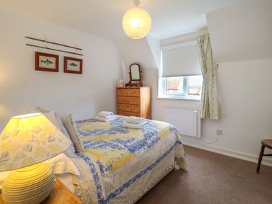 A bedroom with a bed covered by a quilt and pillows two windows a dresser with a mirror and a table lamp at 1 Market Hill in Orford