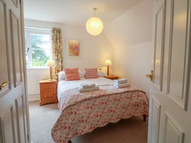 A bedroom with a double bed two bedside tables with lamps a window with floral curtains and folded towels on the bed at 1 Market Hill in Orford