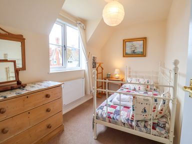 A bedroom with a white metal bed frame a wooden chest of drawers a window and a framed painting at 1 Market Hill in Orford