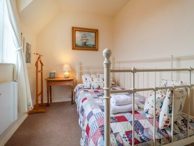 A bedroom with a bed covered in a patchwork quilt and pillows a wooden side table with a lamp a wooden clothes stand a painting of a ship on the wall at 1 Market Hill in Orford