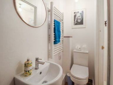 A small bathroom with a sink, a round mirror, a towel rack with a blue towel, a toilet, and a framed picture on the wall at 1 Market Hill in Orford