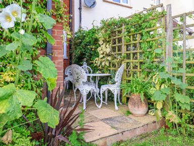 An outdoor patio with white metal table and chairs surrounded by green plants and a trellis at 1 Market Hill in Orford
