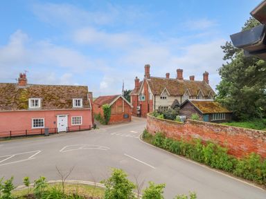 A street view with traditional brick and timber houses and a curved brick wall at 1 Market Hill in Orford