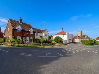 A street view of houses and a church with a flag on a tower at 1 Market Hill in Orford
