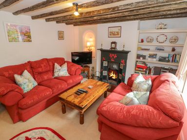 A living room with red sofas a wooden coffee table a fireplace a television and a bookshelf at 4 Lansdown Cottages Bourton-On-The-Water