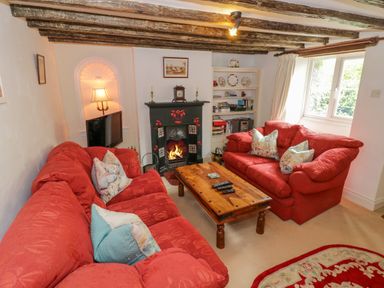 A living room with red sofas wooden coffee table fireplace and bookshelf at 4 Lansdown Cottages Bourton-On-The-Water