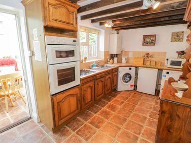 A kitchen with wooden cabinets a double oven a washing machine a small refrigerator and a microwave at 4 Lansdown Cottages Bourton-On-The-Water