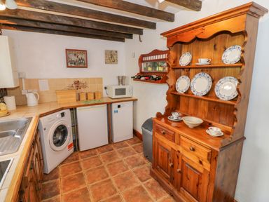 A kitchen with wooden cabinets a washing machine microwave and plates on a wooden dresser at 4 Lansdown Cottages in Bourton-On-The-Water