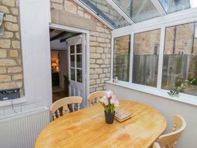 A dining area with a wooden table and chairs inside a conservatory with stone walls at 4 Lansdown Cottages in Bourton-On-The-Water